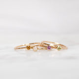 Four yellow gold Birthstone Rings (Citrine, Opal, Pink Tourmaline and Peridot) on a white background. 