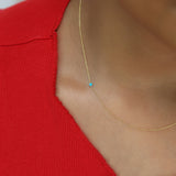 A close-up of a neck wearing a yellow gold 14K Gold Asymmetrical Birthstone Necklace - Turquoise (December), styled in a red top. 