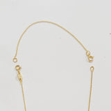 A yellow gold chain extender shown on top of a partially visible yellow gold cable-chain necklace on a light grey background.
