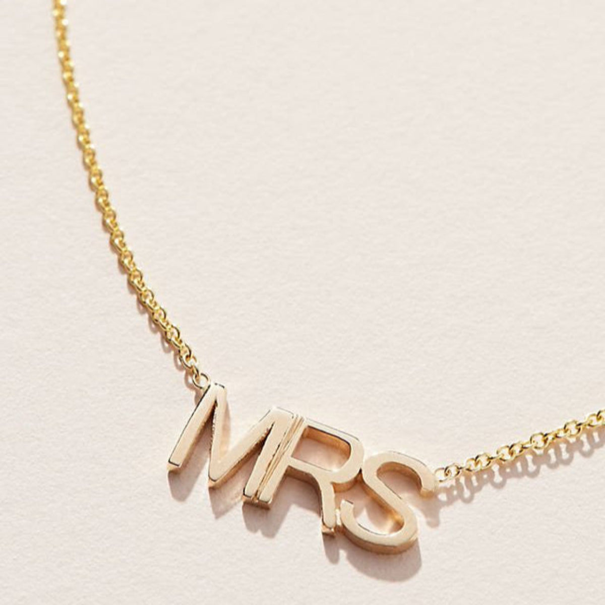 Close-up of a MRS Necklace in yellow gold on a cable chain on an off-white background. 