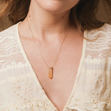 A close-up of a neck wearing The Happiness Retreat Necklace, styled in a low neck light yellow top. 