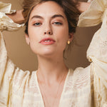 A woman wearing The Clarity Retreat Necklace and Solid Eclipse Earrings - Small, styled with a light yellow long sleeve top against a light brown background. 