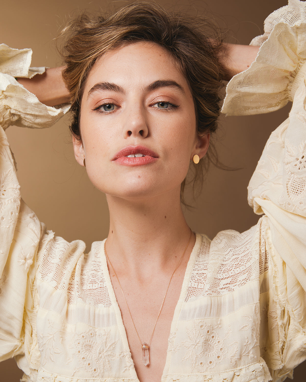 A woman wearing The Clarity Retreat Necklace and Solid Eclipse Earrings - Small, styled with a light yellow long sleeve top against a light brown background. 