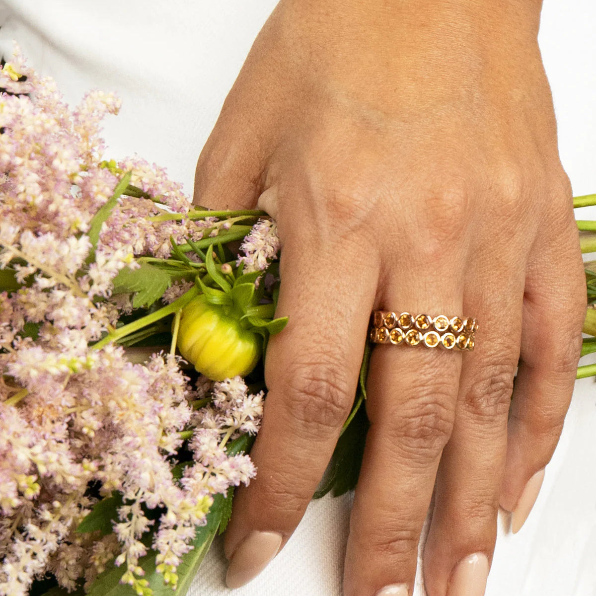 A hand wearing two The Daisy Bouquet Rings and holding a bunch of flowers. 
