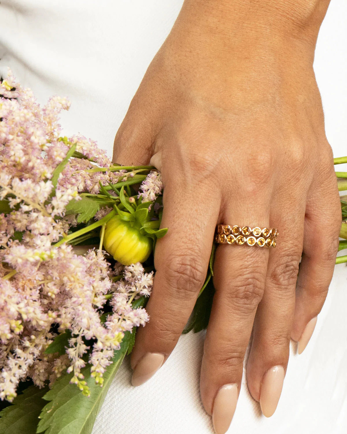 A hand wearing two The Daisy Bouquet Rings and holding a bunch of flowers. 