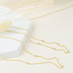 A Triple Diamond Layering Necklace and a Quintet Diamond Layering Necklace in yellow gold laid on a white and nude coloured surface.