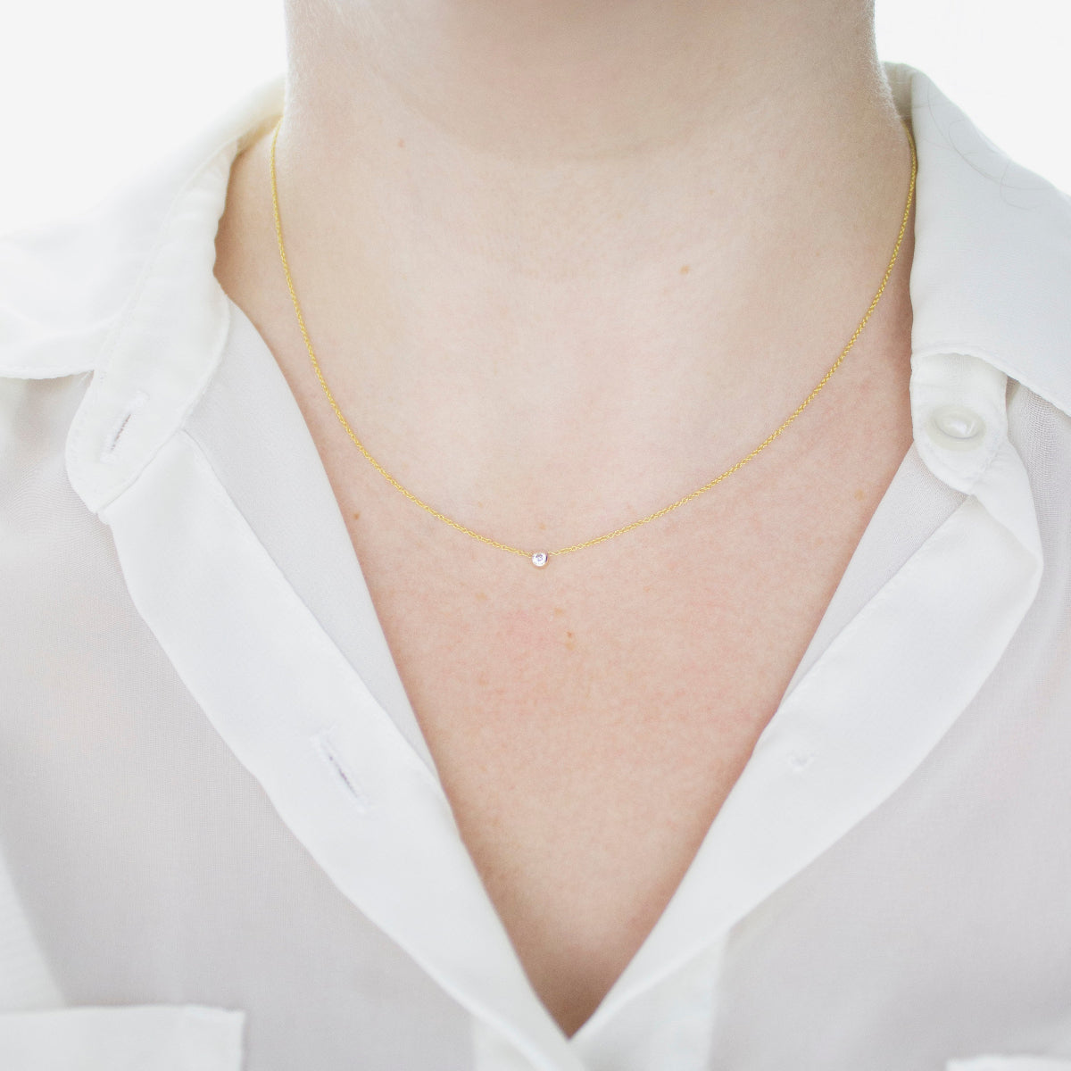 A close-up of a woman's neck wearing a yellow gold Diamond Layering Necklace, styled in a white shirt. 