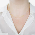 A close-up of a woman's neck wearing a yellow gold Diamond Layering Necklace, styled in a white shirt. 