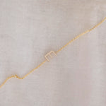 A yellow gold necklace with a letter E charm, displayed diagonally on a cream fabric background.