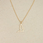 An England pendant necklace in yellow gold with a beaded chain on a beige fabric background. 