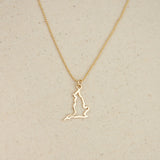 An England pendant necklace in yellow gold with a beaded chain on a beige fabric background. 