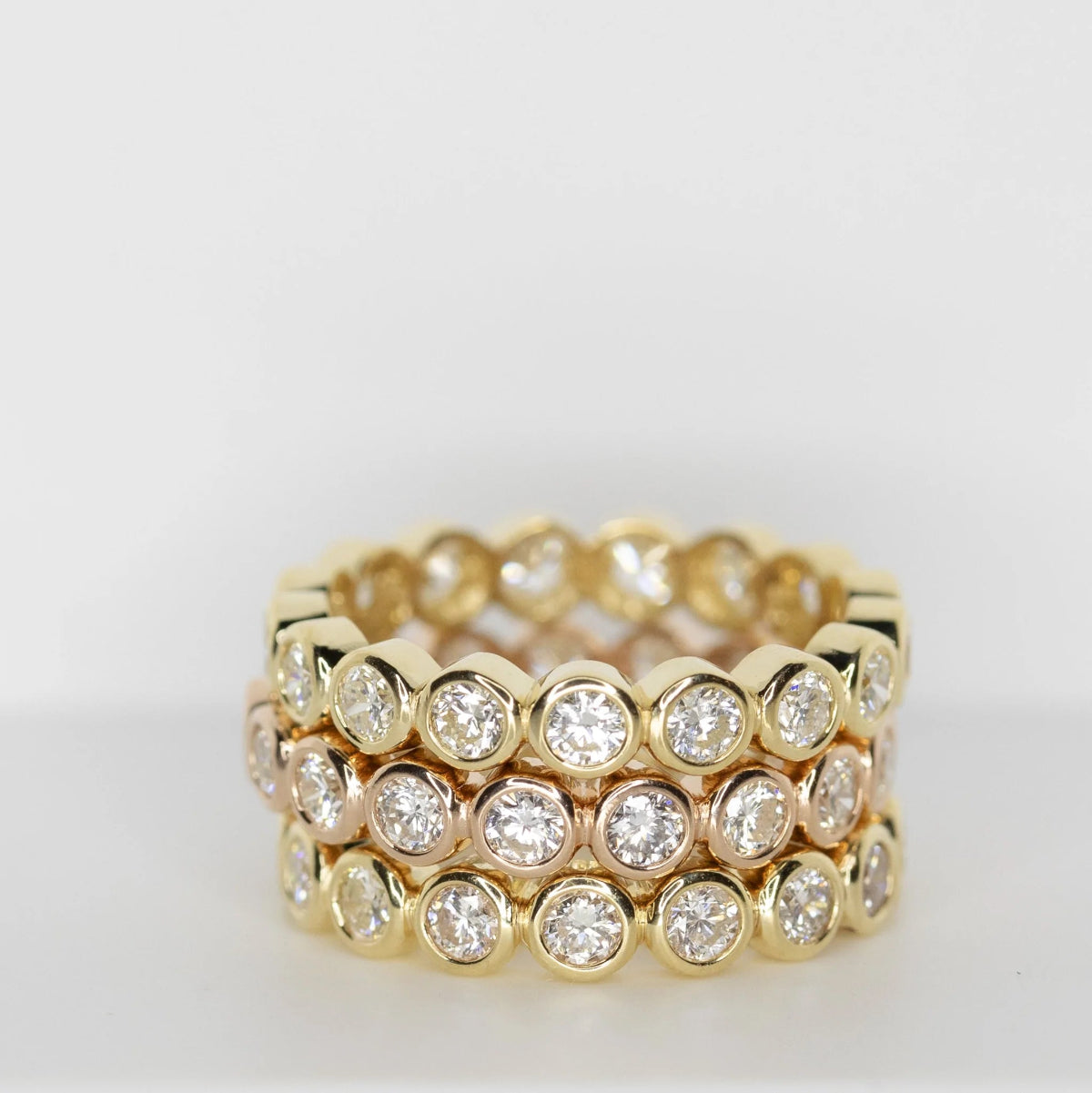 Three yellow gold The Evermore Rings against a light grey background. 