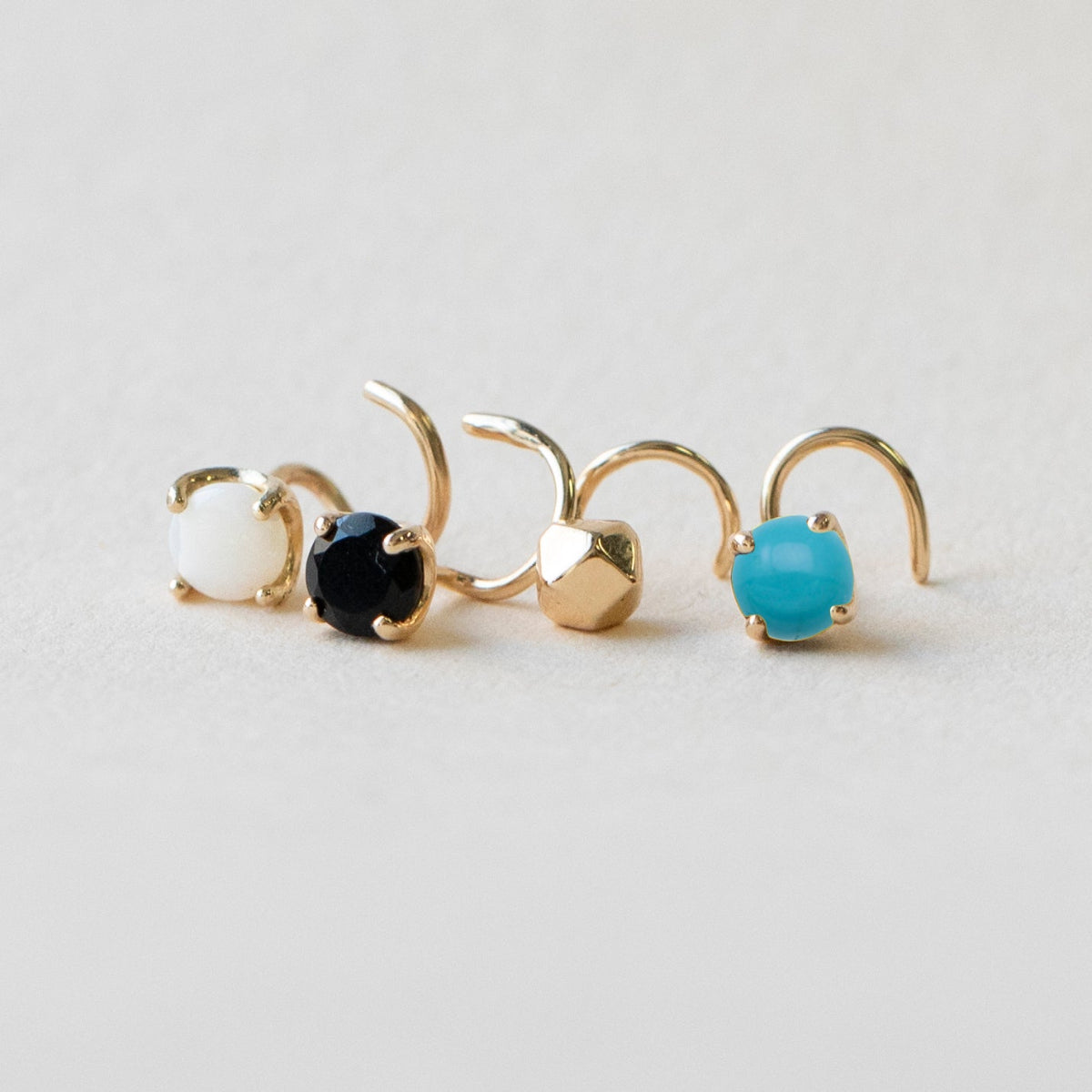 An Alli Webb Faceted Comfort Stud, Turquoise Comfort Stud, Opal Comfort Stud and Opal Comfort Stud on a light grey surface.