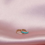 An Alli Webb Opal Huggie and Turquoise Huggie on a light pink silk fabric. 