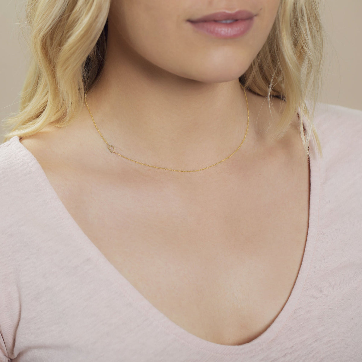 A close-up of a woman's neck wearing a yellow gold necklace with a letter D charm.