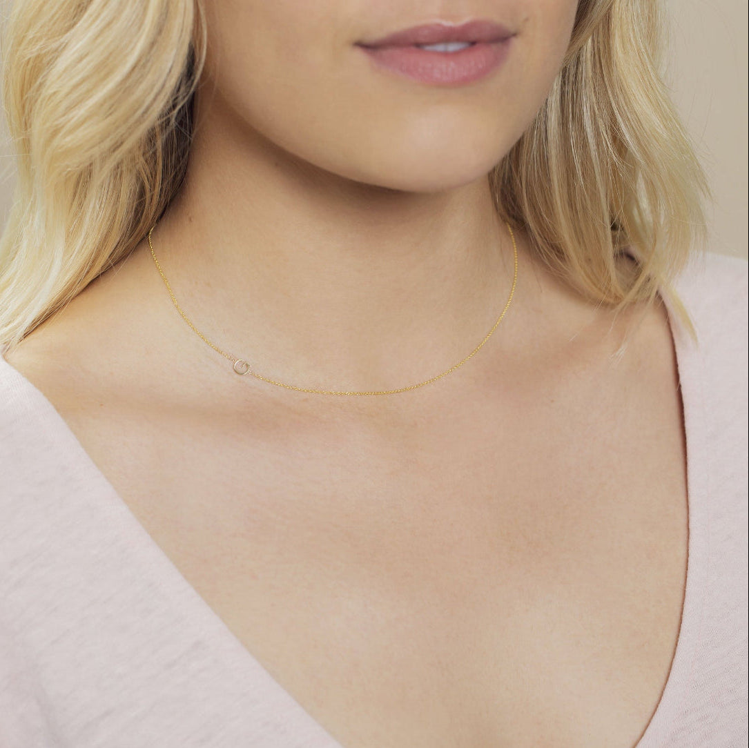 Close-up of a woman's neck wearing a gold necklace with a letter G charm. 