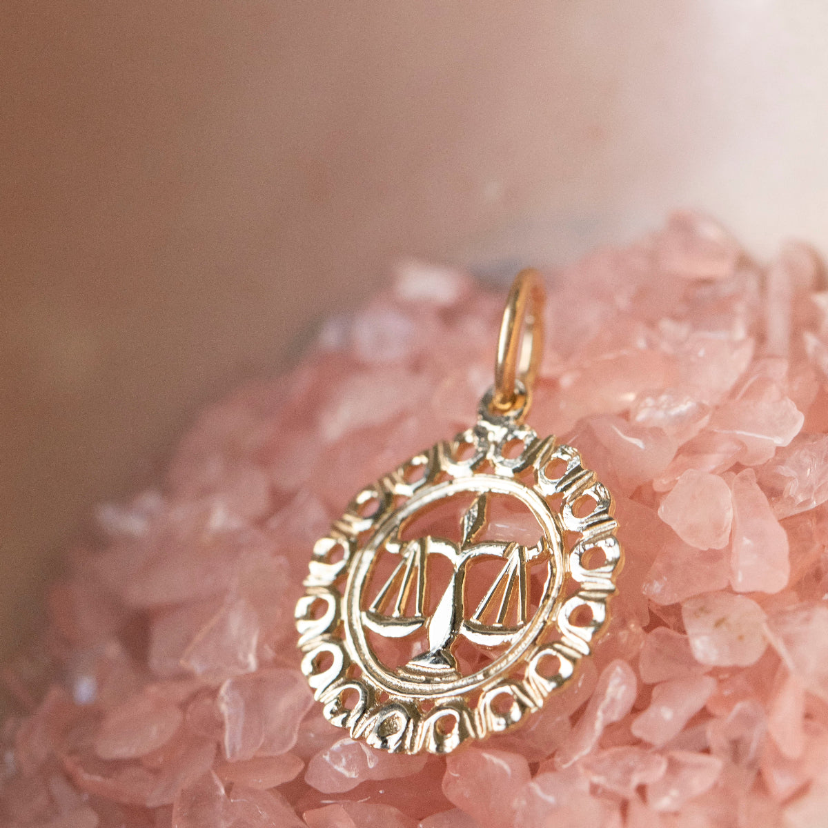 The Zodiac Necklace - Libra pendant laid on top of pink crystals.