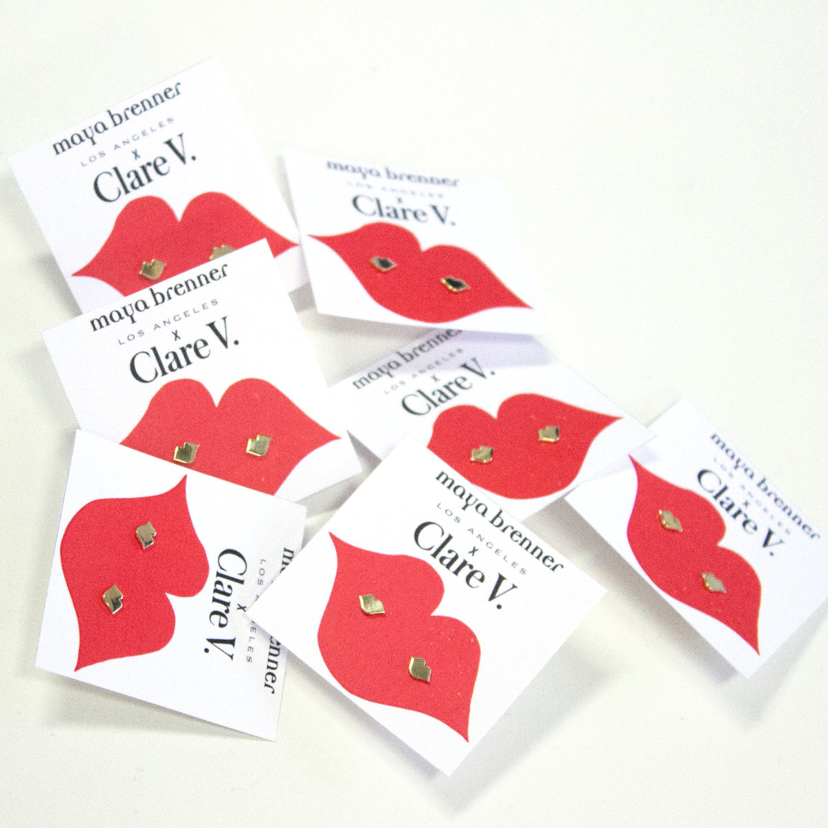 Various Lip Studs on white cards with Maya Brenner x Clare V and red lips against an off-white background. 