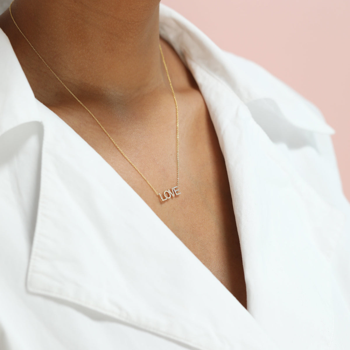 A LOVE Necklace in yellow gold on a cable chain on a white background. 