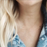 A close-up of a woman's neck wearing a yellow gold necklace with a letter R charm. 