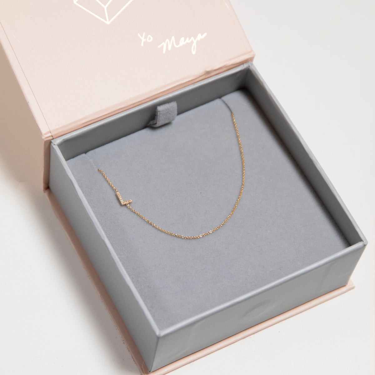 A yellow gold necklace with a pave letter L charm in a jewelry box. 