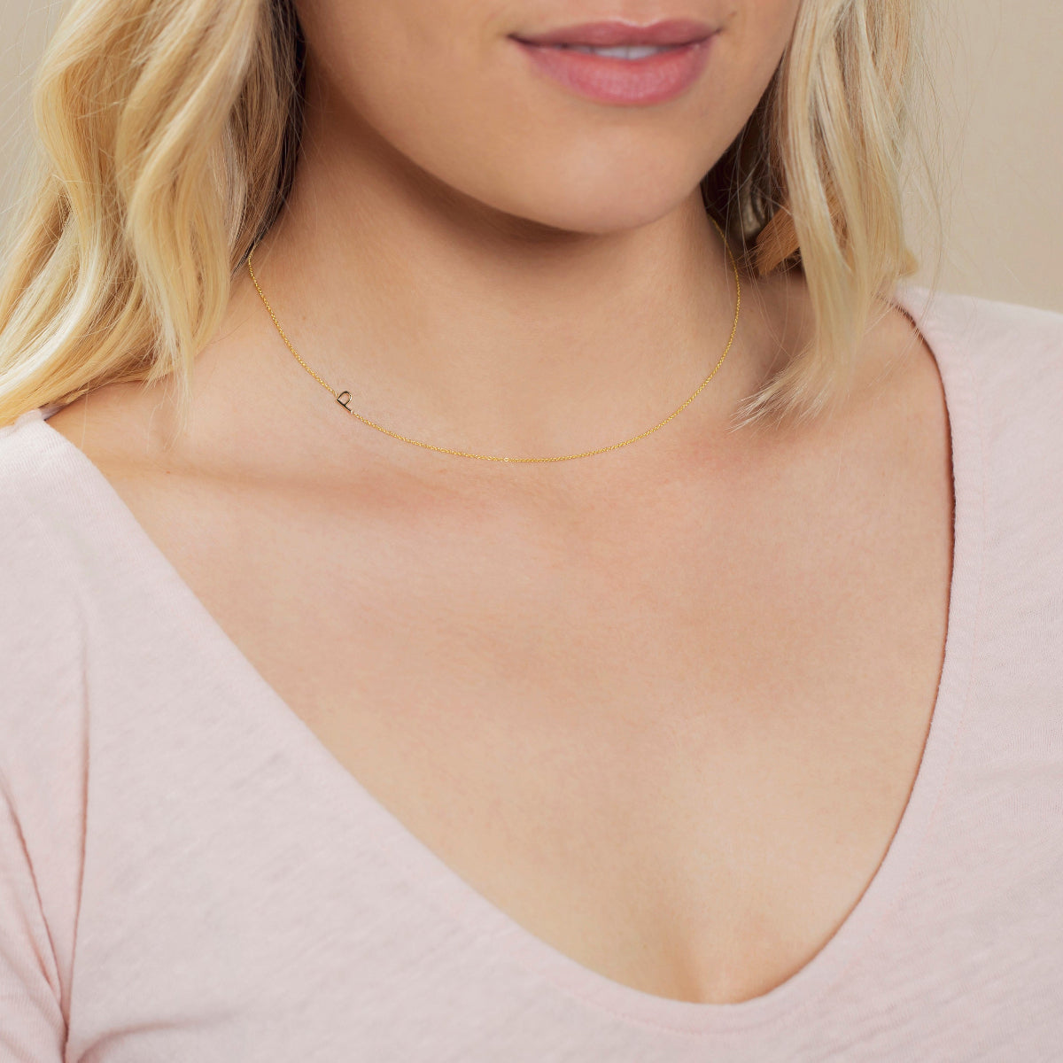 A close-up of a woman's neck wearing a yellow gold necklace with a letter P charm. 