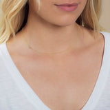A close-up of a woman's neck wearing a 14k Gold Asymmetrical Number Necklace - 4 in yellow gold, styled with blonde hair and a white top.