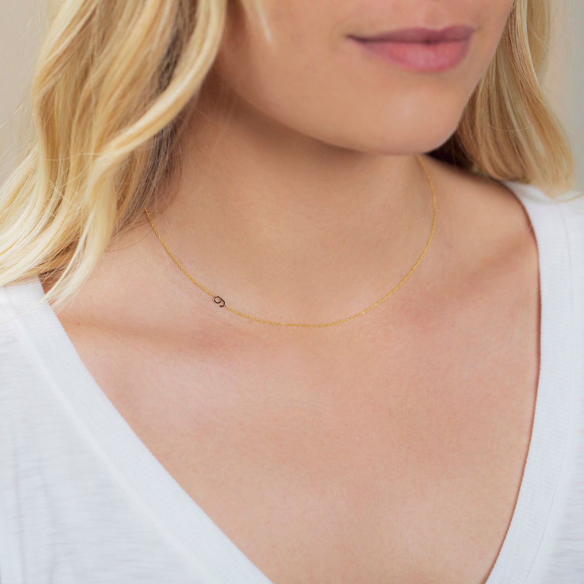 A close-up of a woman's neck wearing a 14k Gold Asymmetrical Number Necklace - 9 in yellow gold, styled with blonde hair and a white top.