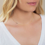 A close-up of a woman's neck wearing a 14k Gold Asymmetrical Number Necklace - 9 in yellow gold, styled with blonde hair and a white top.