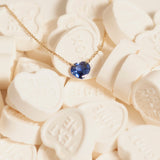 The Sweetheart Necklace - Blue Sapphire in yellow gold laid on top of white heart-shaped candy. 