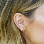 Close-up of a woman's ear wearing an Alli Webb Faceted Huggie and Onyx Huggie, with her blonde hair visible. 