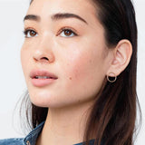 Close-up of a woman wearing a yellow gold Open Eclipse Earring - Large, with brown hair against a light grey background. 
