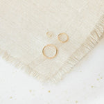 Open Eclipse Earrings (mini, small, and large) in yellow gold on a cream fabric and white speckled surface.