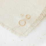 Open Eclipse Earrings (mini, small, and large) in yellow gold on a cream fabric and white speckled surface.
