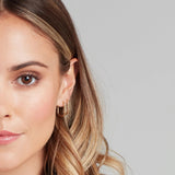 Close-up of a woman wearing two Oval Hoops in yellow gold against a light grey background. 
