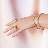 A hand wearing a yellow gold Paris Ring, Etched Paris Ring and two Rolo Bracelets against a blurred background. 