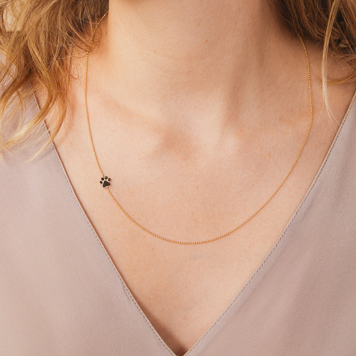 A close-up of a woman's neck wearing a yellow gold 14k Gold Asymmetrical Charm Necklace - Paw with a cable chain, styled with neutral top. 