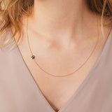 A close-up of a woman's neck wearing a yellow gold 14k Gold Asymmetrical Charm Necklace - Paw with a cable chain, styled with neutral top. 