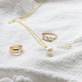 A Tres Pearl Ring, Perla Ring, Perla Necklace and a Tres Pearl Earring on white fabric. 