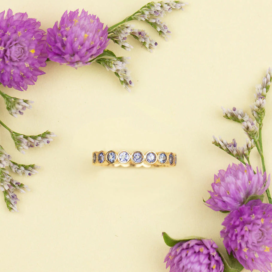 The Periwinkle Bouquet Ring on a light yellow background with purple flowers in two corners.