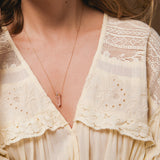 Close-up of a woman's décolletage wearing The Love Retreat Necklace, with a light yellow frilly top. 