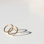 A pair of Open Eclipse Earrings - Small in yellow gold against a light grey background. 