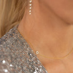 A close-up of a woman's neck wearing a 14k Gold Asymmetrical Charm Necklace - Star of David in yellow gold with a cable chain, along with Diamond Cascade Earrings, styled with a silver sequined top.