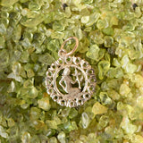 The Zodiac Necklace - Virgo pendant laid on top of green clear stones. 