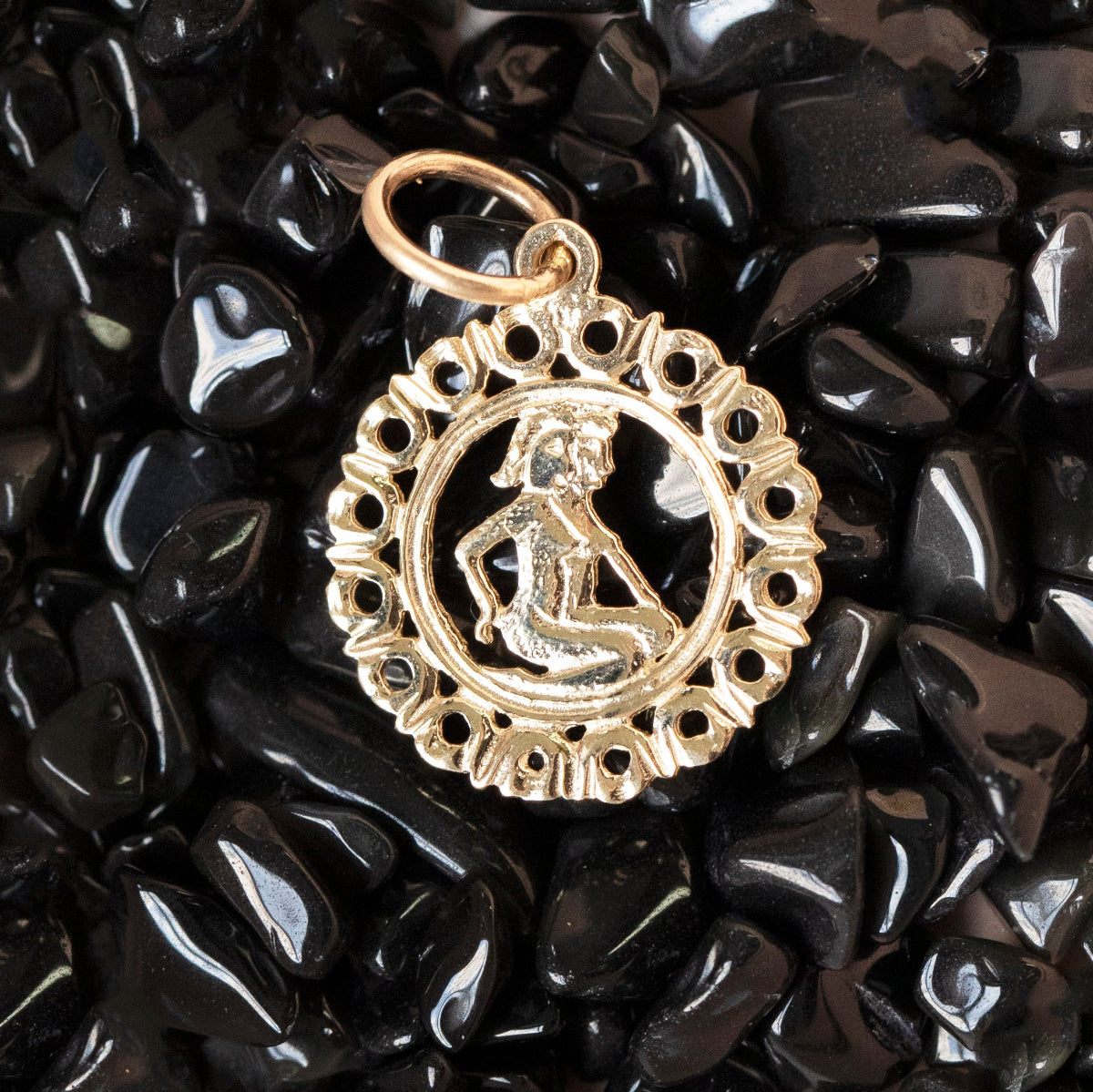 The Zodiac Necklace - Gemini pendant laid on top of black stones. 