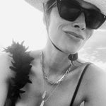 A black and white photo of Abigail Spencer wearing a Bold Link Chain and two Retreat Necklaces, along with black sunglasses, a black top and a sun hat.