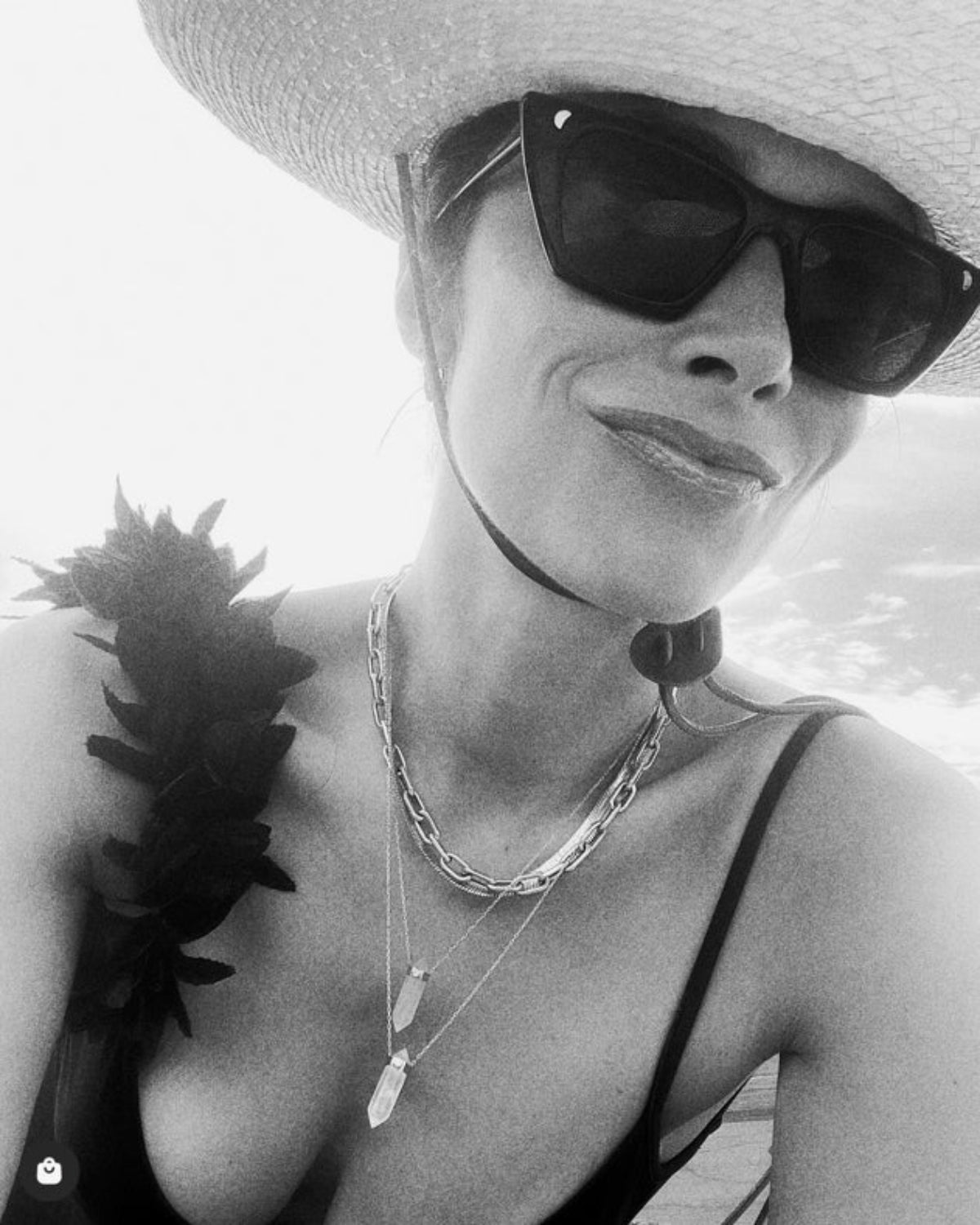 A black and white photo of Abigail Spencer wearing a Bold Link Chain and two Retreat Necklaces, along with black sunglasses, a black top and a sun hat.