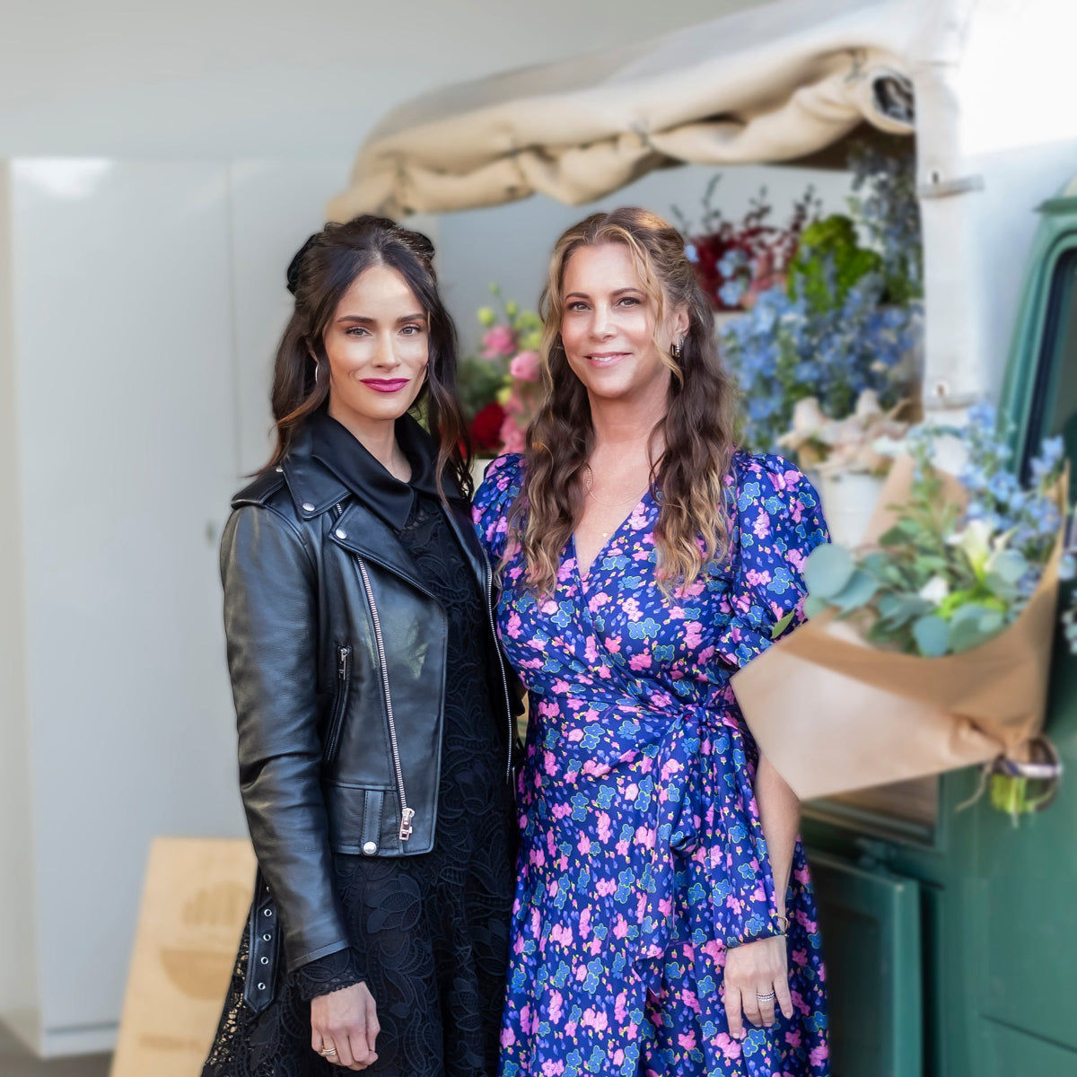 Abigail Spencer and Maya Brenner standing in front of a floral delivery truck in the background. 