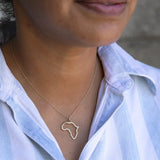 Close-up of a person's neck wearing an Africa necklace in sterling silver with a blue and white striped shirt against a grey blurred background. 