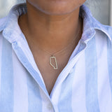 Close-up of a person's neck wearing an Alberta necklace with a blue and white striped shirt against a grey blurred background. 